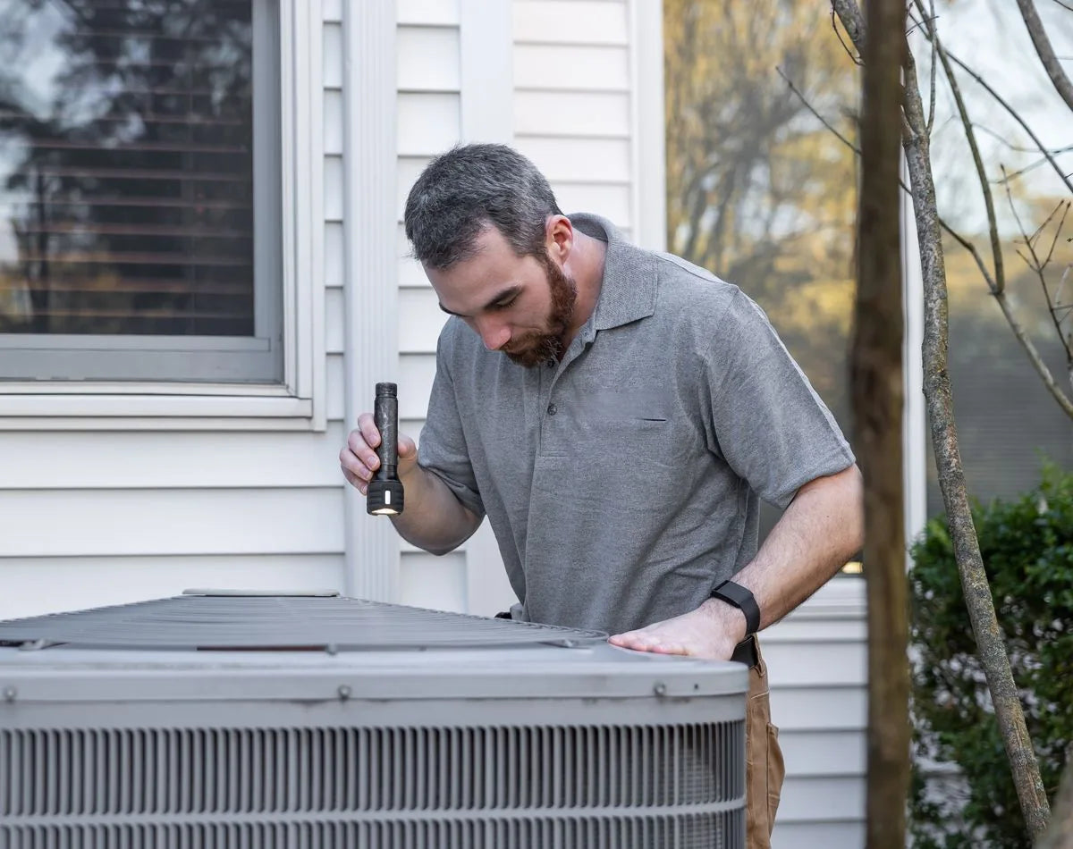 Technician inspecting an outdoor air conditioning unit at a home